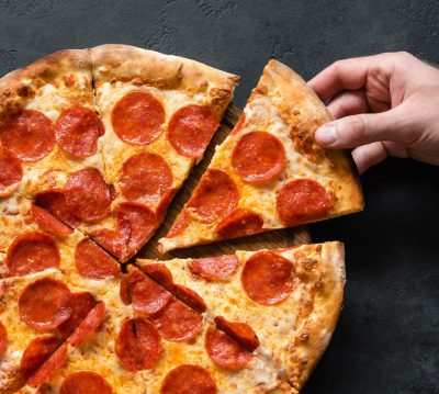 Hand picking slice of pepperoni pizza